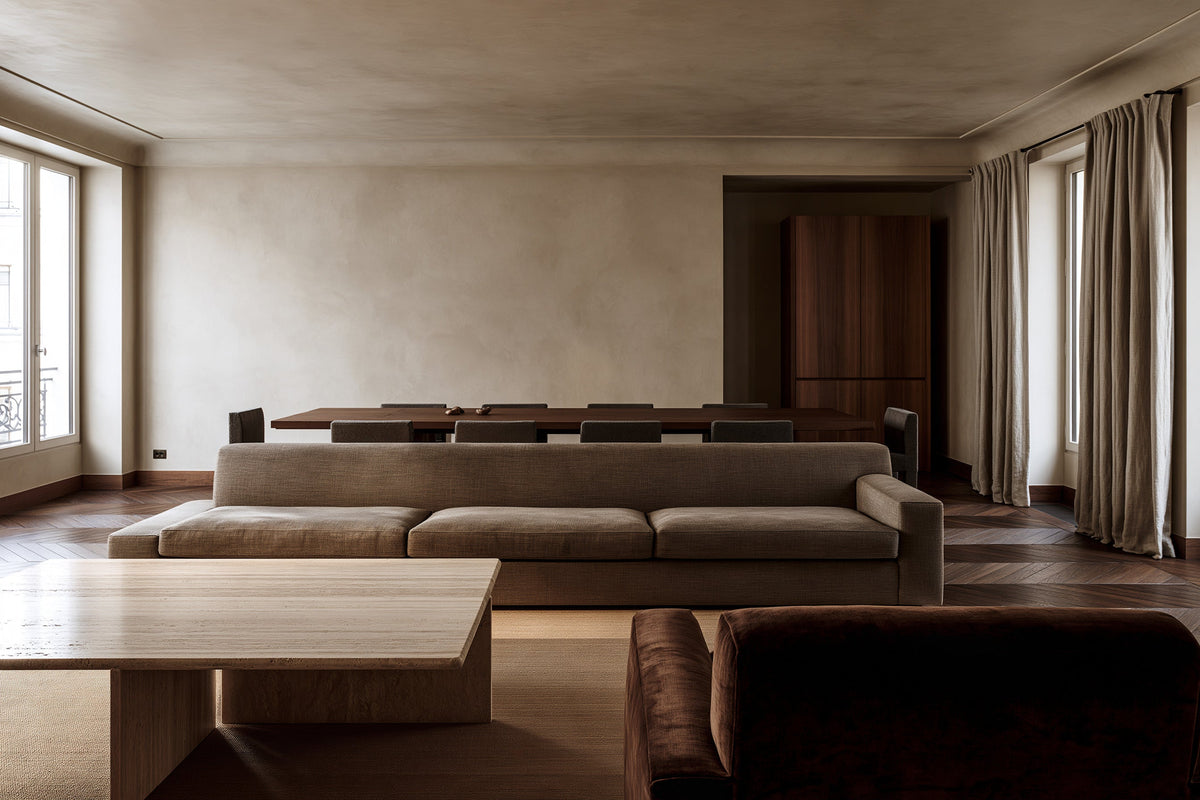 An open living and dining room in a Paris apartment with a taupe sofa and a travertine table